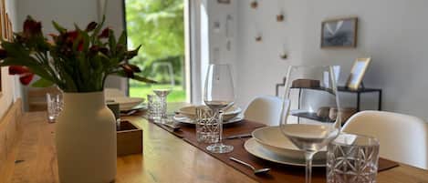 A dining table set with plates, glasses, and cutlery, a vase with flowers, and a view of greenery outside.