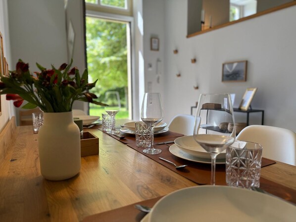 A dining table set with plates, glasses, and cutlery, a vase with flowers, and a view of greenery outside.