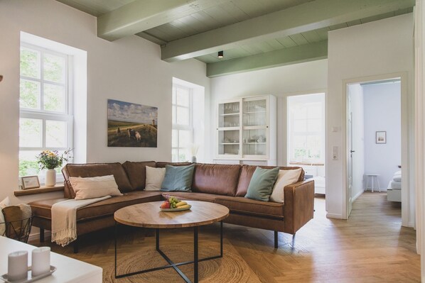 A spacious living room with a brown leather sectional sofa, a round coffee table, and a painting on the wall.