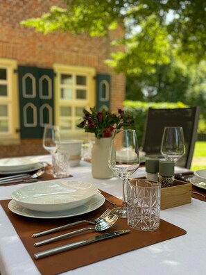 A table set outdoors with plates, cutlery, glasses, and a vase of flowers.