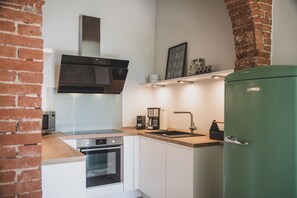 A compact kitchen with a built-in oven, a microwave, a gas stove, a stainless steel range hood, a sink, and a green refrigerator.