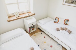 A child's bedroom with a bunk bed, a nightstand with books, a colorful rug, and a window with a view.