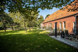 A brick building with a tiled roof, a grassy lawn, and a patio with outdoor furniture.