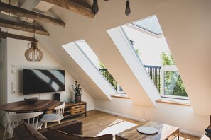 En modern loftlägenhet med en stor TV, ett matbord i trä och en mysig sittgrupp.
