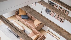 Un interior moderno con una escalera de madera, un conjunto de sofás y una zona de comedor.