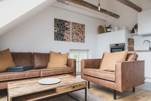 Un salon moderne avec un canapé en cuir marron, une table basse en bois et des œuvres d’art abstraites accrochées au mur.