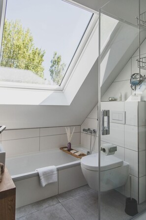 Une salle de bain moderne dotée d’une lucarne, d’une baignoire, de toilettes et d’un espace douche.