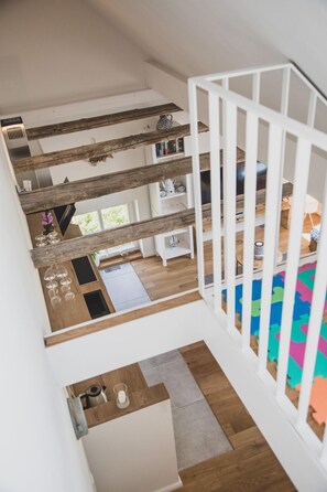 Um interior moderno com escada de madeira, vista para uma sala de estar com sofá e mesa de centro, e um tapete colorido no chão.