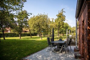 Un patio exterior con una mesa y sillas, rodeado de un césped cuidado y árboles.
