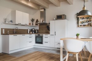 Eine moderne Küche mit weißen Schränken, einem eingebauten Backofen und einer Mikrowelle auf der Kühlmaschine. Es gibt eine Holz Arbeitsplatte, ein Spülbecken und einen Essbereich mit Tisch und Stühlen.