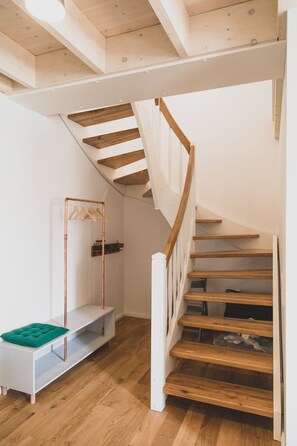 Eine Holztreppe mit weißen Geländern und einer weißen Wand, an der ein Kleiderständer hängt.