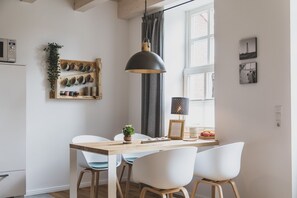 Eine moderne Küche mit einem Holztisch, weißen Stühlen, einer abgehängten Topfhalterung und einer Pendelleuchte.