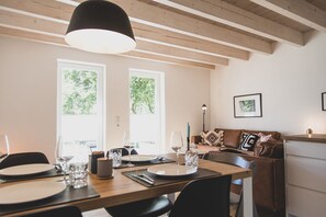 Uma área de refeições com mesa de madeira posta para dois, um sofá e um abajur.