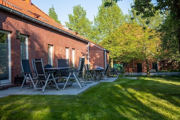 A brick building with a tiled roof, outdoor seating with metal chairs and a table, and a well-maintained lawn.