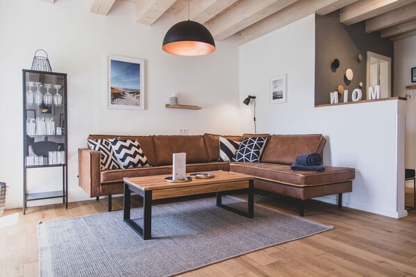 A modern living room with a brown leather sofa, a wooden coffee table, and a black pendant light.