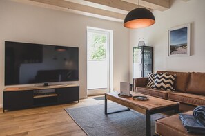 Ein modernes Wohnzimmer mit einem großen Flachbildfernseher, einem Holztisch, einem braunen Ledersofa und einer schwarzen Pendelleuchte.