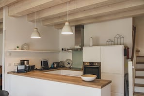 A modern kitchen with wooden beams, white cabinetry, and pendant lighting.