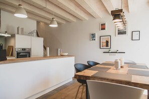 A modern kitchen with a wooden countertop, white cabinets, and a dining area with a wooden table and chairs. - Exklusive Maisonette Ferienwohnung "aafke" im Gulfhof mit Sauna und Wunderschönen Obstgarten - (Krummhörn)