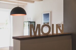Ein Empfangsschalter mit hölzernen Lettern, die 'MOIN' buchstabieren, und einer Pendelleuchte darüber.