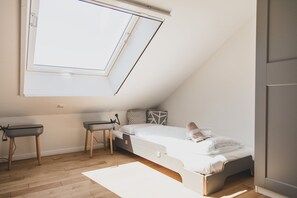 Ein gemütliches Schlafzimmer mit schrägen Wänden, einem Einzelbett, einem kleinen Schreibtisch und einem Fenster für natürliches Licht.