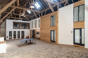 A spacious indoor area with a ping pong table, wooden panel walls, and a high ceiling with exposed beams.