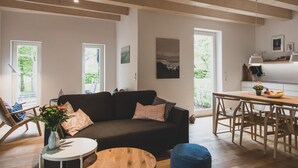 Una sala de estar moderna con un sofá oscuro, una mesa redonda de madera y una zona de comedor con un banco de madera.