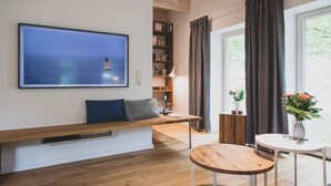 Una sala de estar moderna con un ventanal grande, un banco de madera con cojines, una mesa redonda de madera y una estantería.