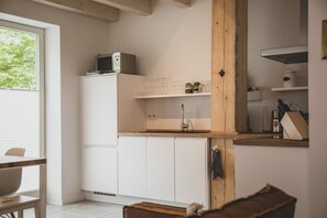 A compact kitchen with white cabinets, a wooden beam, a microwave, and a sink.