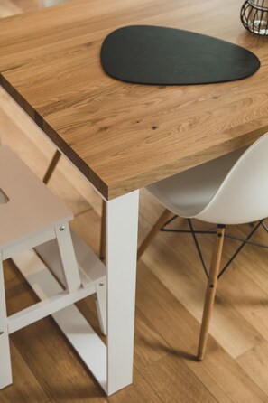 Ein Holztisch mit einer schwarzen Tischmatte, einem weißen Stuhl und einem Drahtkorb darauf.