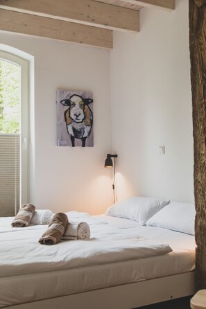 A bedroom with a bed, a painting of a sheep, a lamp, and a window.