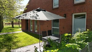 A patio area with a table and chairs under a large umbrella, adjacent to a brick building with windows and a garage door.