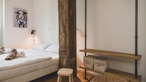 Quarto com cama, vigas de madeira, prateleira com caixas organizadoras e ar condicionado fixado na parede.
