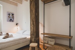Ein Schlafzimmer mit einem Bett, einem Holzbalken, einem Regal mit Aufbewahrungsbehältern und einer Wand-Klimaanlage.