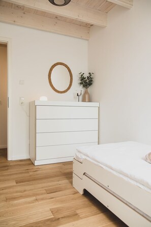 Ein Schlafzimmer mit weißem Schminktisch, einem Bett, Holzboden und einem an der Wand befestigten Spiegel.