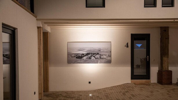 Um corredor com uma fotografia em preto e branco na parede, uma porta com painel de vidro e piso de tijolos.