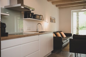 A modern kitchen with white cabinets, a wooden countertop, a black coffee machine, and a black sofa in the adjacent living area.