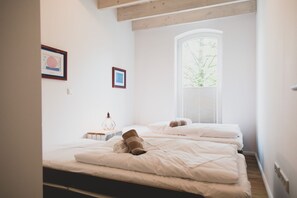 A bedroom with two beds, a window with blinds, and a geometric light fixture.