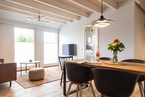 A modern dining area with a wooden table, black chairs, and a hanging light fixture. - Wunderschöne Wohnung "hinrich" - Gulfhof Boomgaarden (Krummhörn)
