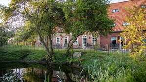 Ein Gebäude aus Ziegeln mit rotem Ziegeldach, umgeben von Bäumen und einem kleinen Teich.