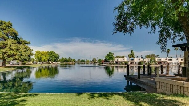 A serene water body with a dock, surrounded by greenery and buildings in the background. - Renovated Villa in Old Litchfield (Litchfield Park)