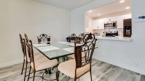 A dining area with a glass table and cushioned chairs, a kitchen with white cabinets and modern appliances, and a light-colored floor. - Renovated Villa in Old Litchfield (Litchfield Park)