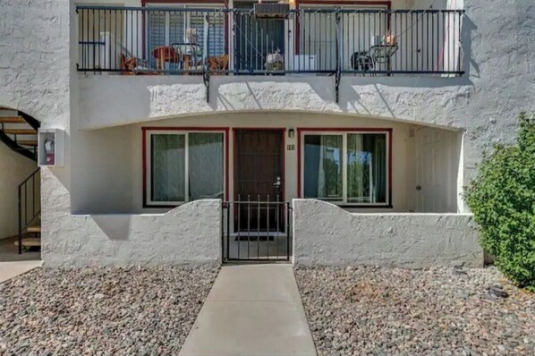 A two-story building with a white exterior, a gated entrance, and a balcony with outdoor furniture.
