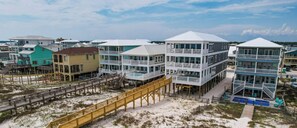 A coastal hotel with multiple stories, balconies, and a wooden boardwalk leading to the beach.