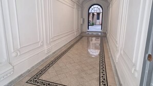 Un couloir aux murs blancs, doté d’un sol en marbre et orné d’un tapis à motifs.
