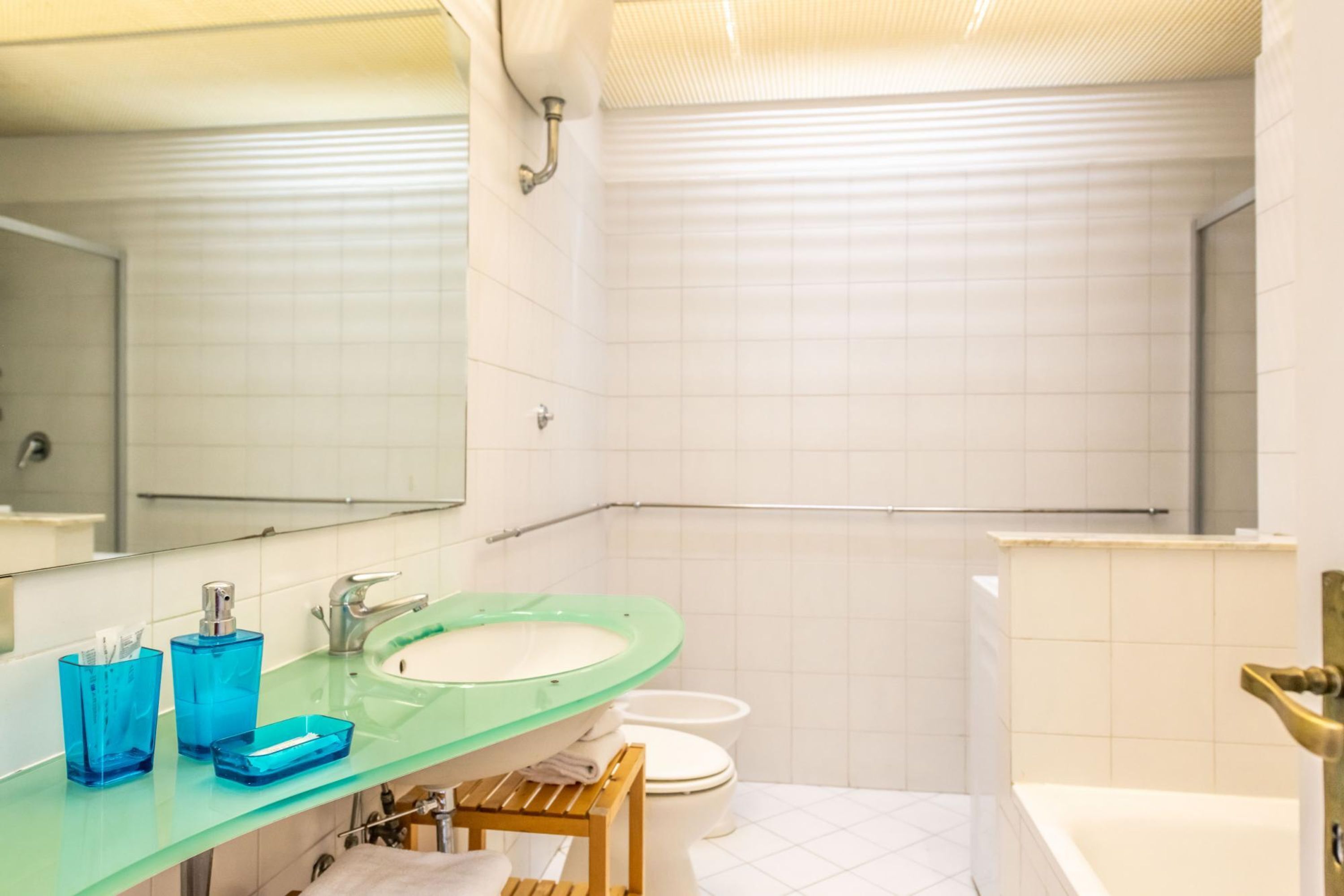 A bathroom with a green glass sink, white tiles, a white toilet, and a bathtub.