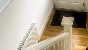 Una escalera con barandilla blanca, una puerta blanca con manija y un felpudo negro al final.