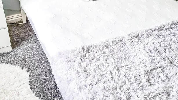 Una cama con una colcha blanca, un plaid gris suave y dos almohadas con un diseño de ciervo.