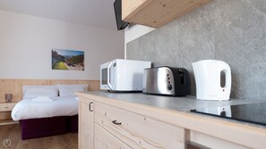 Une cuisine moderne équipée d’un four à micro-ondes, d’un grille-pain et d’une bouilloire sur le plan de travail, un lit avec une literie blanche et un tableau accroché au mur.