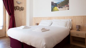 Una cama bien tendida con sábanas y toallas blancas, cabecera de madera y una mesita de noche con una lámpara.