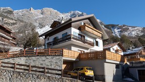 Un edificio de varios pisos con balcones, un muro de piedra y un coche amarillo estacionado en la entrada.